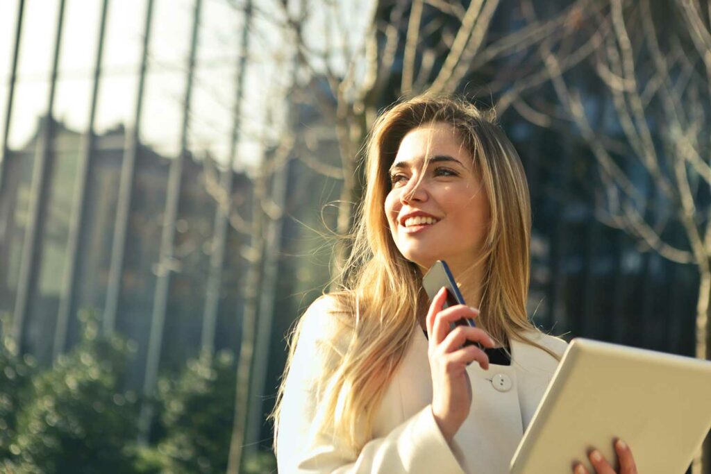 a woman outside with a folder in one hand and her phone in the other, looking to the left